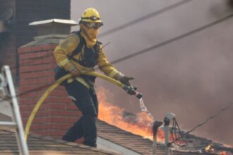 A cropped Cal Fire photo of a firefighter on a rooftop during the 2025 Palisades Fire.