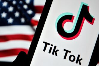 A phone displaying the TikTok logo in front of the US flag.